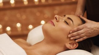 Woman with eyes closed, lying down, getting a head massage.