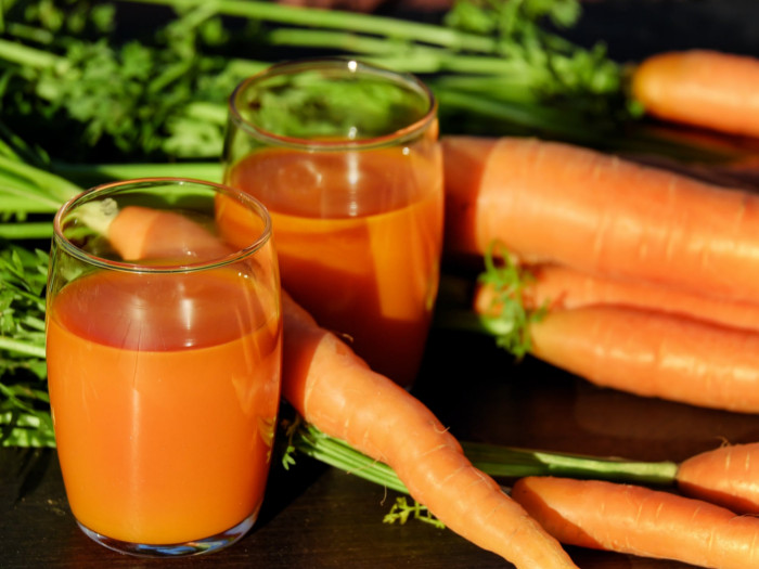 Two glasses of fresh carrot juice kept beside carrots atop a wooden table