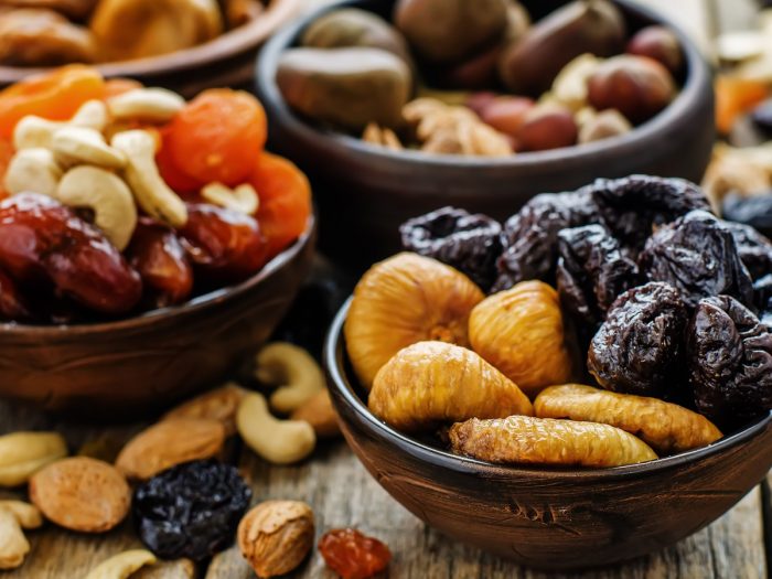 Mini bowls filled with dry fruits such as figs, prunes, cashews, and other nuts