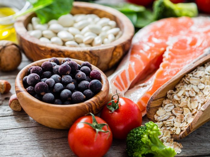 Healthy foods like salmon, oats, berries, nuts and tomatoes on a wooden counter