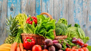 A basket of healthy vegetables and fruits (red bell pepper, tomatoes, carrots, pineapple, beetroots, banana, lettuce, spinach, broccoli) on a wooden table