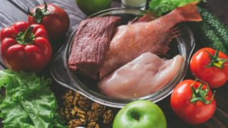 Healthy foods for weight gain (raw chicken, fish, pork, tomatoes, red chilies, apples, cucumbers, eggs, spinach, milk, and apricots) on a wooden table