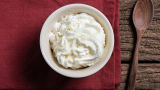 Heavy whipped cream in a white bowl on a red napkin, next to a wooden spoon