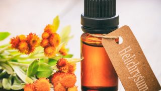 A small bottle of helichrysum essential oil with helichrysum flowers on a wooden table