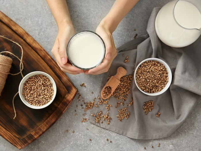 A hand holding milk in a glass and two bowls of hemp seeds around