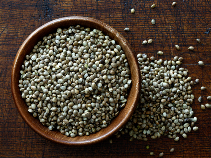A wooden bowl filled with dried hemp seeds and scattered on a wooden table