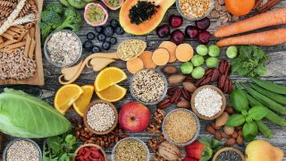 Many high fiber foods including whole wheat pastas, fruits, vegetables, nuts on a wooden counter