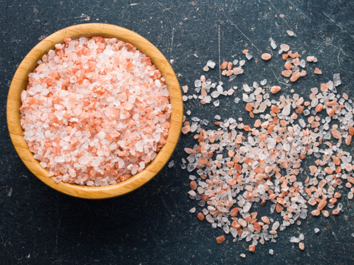 Pink Himalayan salt in and outside of a bowl over a black background