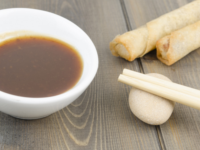 Hoisin sauce in a white bowl, chopsticks, and spring rolls kept on a wooden background