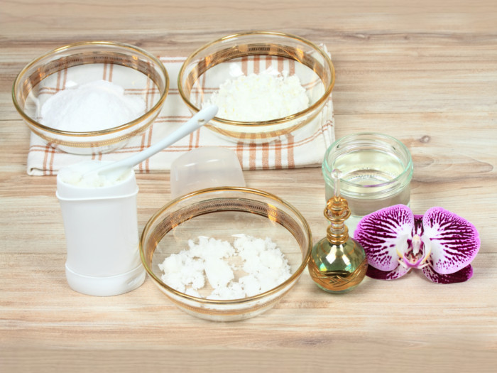 Three bowls containing white powder, flower, bottle, dispenser, placed on a wooden surface.