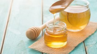 Two glass jars filled with honey, a honey dipper, and a wooden spoon filled with the golden liquid