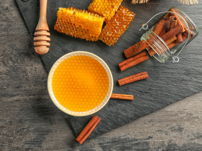 A bowl of honey, honeycomb and a jar of cinnamon sticks on a wooden table