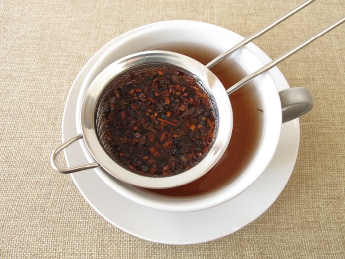 A cup of honey bush tea with a tea strainer on the brim of the cup