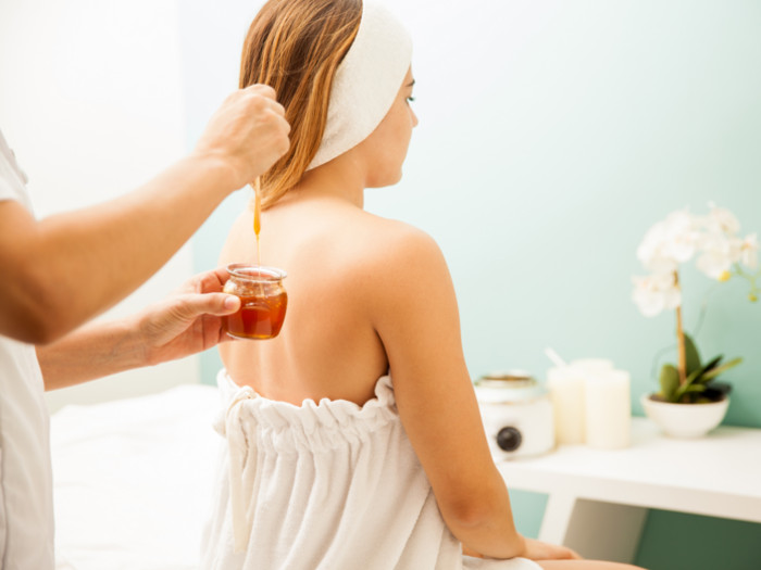 Back View of a woman and someone dipping her hair ends in a jar of honey.