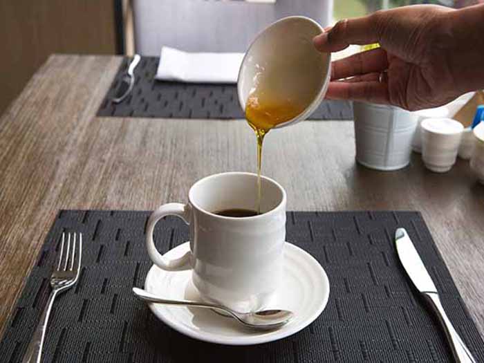 A person pouring honey in coffee