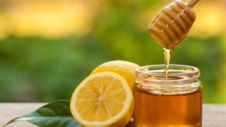 A jar of honey and a half-cut lemon with a leaf beside