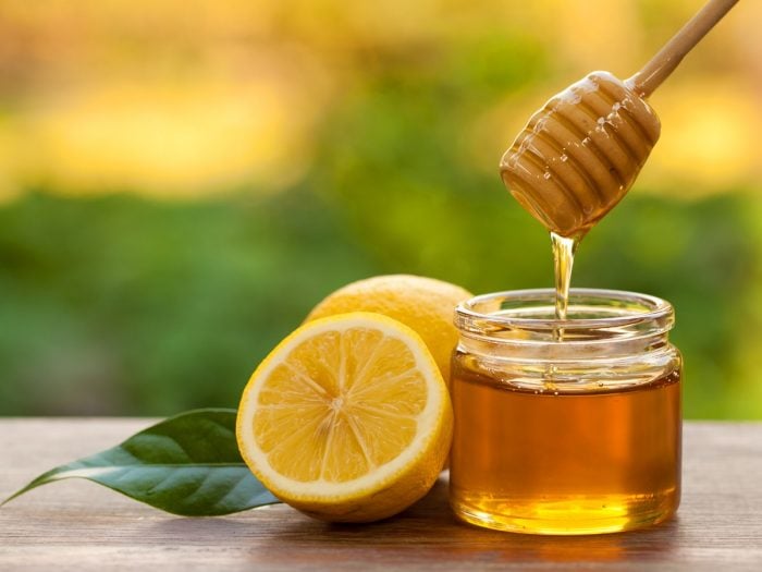 A jar of honey and a half-cut lemon with a leaf beside
