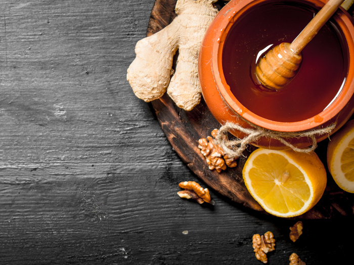 A pot of honey with fresh cut lemon and ginger at the side