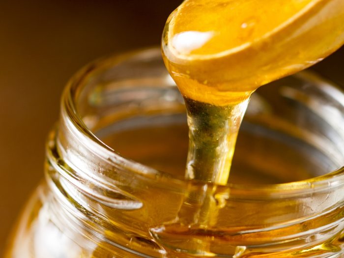 Extreme closeup of a spoon dripping a very viscous golden-colored liquid into a jar.