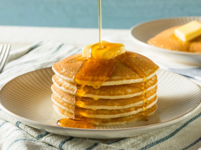 Honey falling on stack of pancakes topped with a small piece of butter