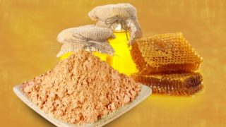 Honey powder on a white dish next to a honeycomb and honey bottles