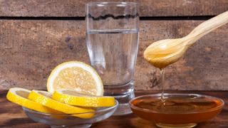 A glass of water, flat bowl of sliced citrus fruits, and a bowl of honey on a rustic background.