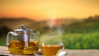 A hot cup of tea with tea pot against a beautiful backdrop