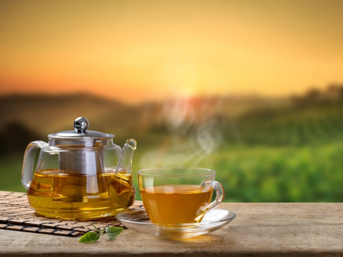 A hot cup of tea with tea pot against a beautiful backdrop