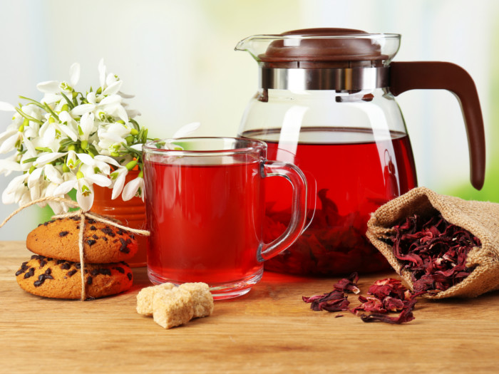 Hibiscus tea in a kettle and a teacup alongside cookies and flowers