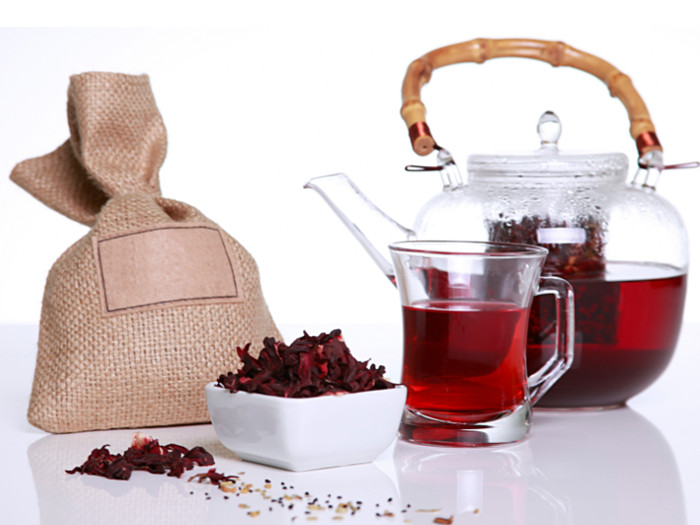 Hibiscus tea in a glass, jar and dried hibiscus flowers on a table