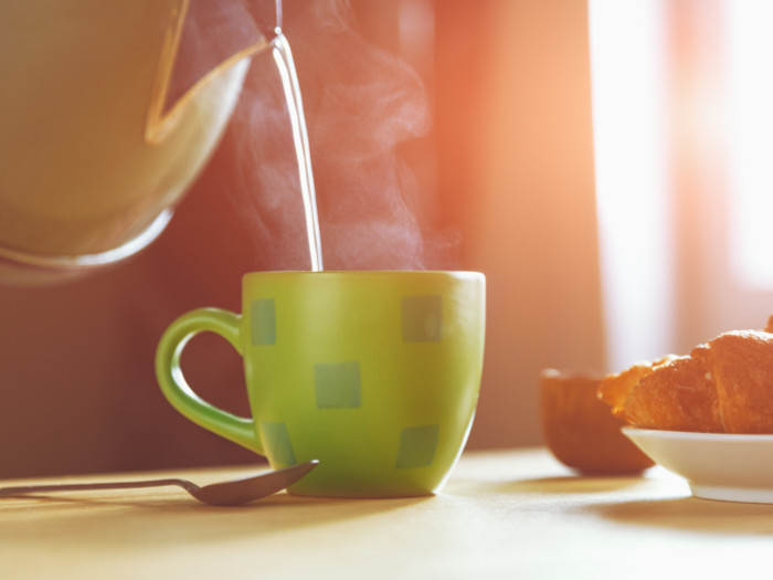 Kettle pouring hot steaming water into a cup in a yellow filter