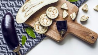 Whole as well as halved, and sliced eggplant on a wooden board on a tablecloth