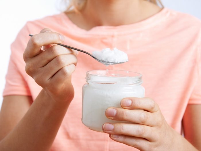 Close up of a young woman with a bottle and spoonful of coconut oil