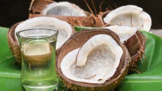 Dry coconut meat in coconut shells on a banana leaf, next to a coconut oil bottle
