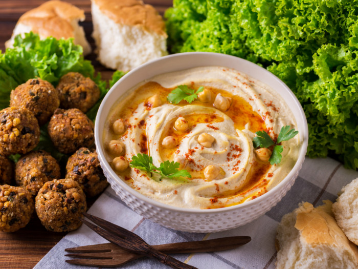 A bowl of hummus, next to salad leaves, falafel, and bread