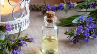 A bottle of hyssop essential oil with fresh hyssop flowers on a wooden table