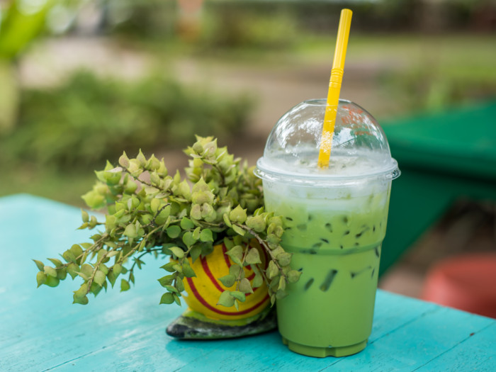 Green liquid in a plastic glass next to a potted succulent, placed on a turquoise-colored table.