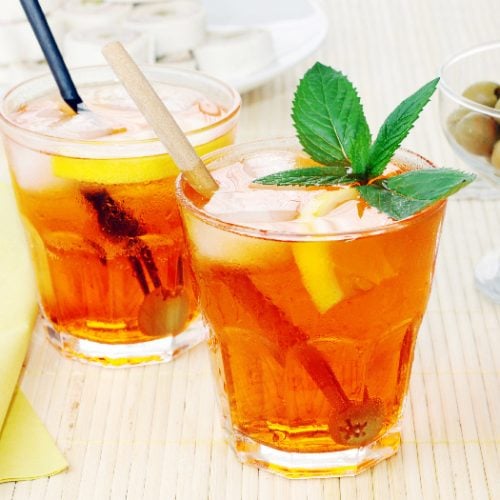 Two small glasses filled with iced tea infused with fruits and mint