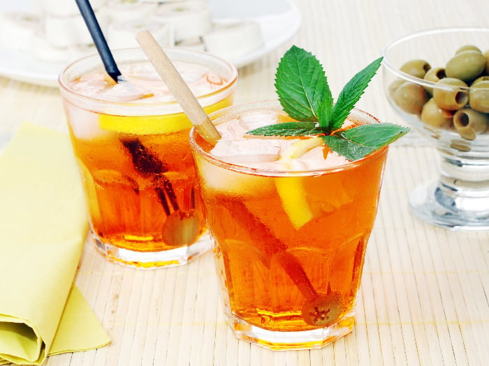 Two small glasses filled with iced tea infused with fruits and mint