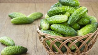 A basket filled with fresh green cucumbers on a wooden table