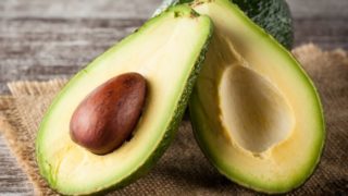Close up of a halved avocado, resting on a whole avocado on burlap