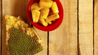 A red bowl of fresh jackfruit next to an empty jackfruit wedge