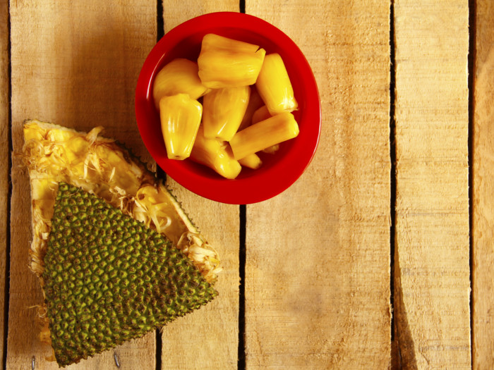 A red bowl of fresh jackfruit next to an empty jackfruit wedge