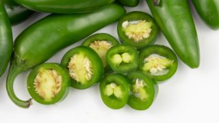 Whole and sliced jalapenos on a white background