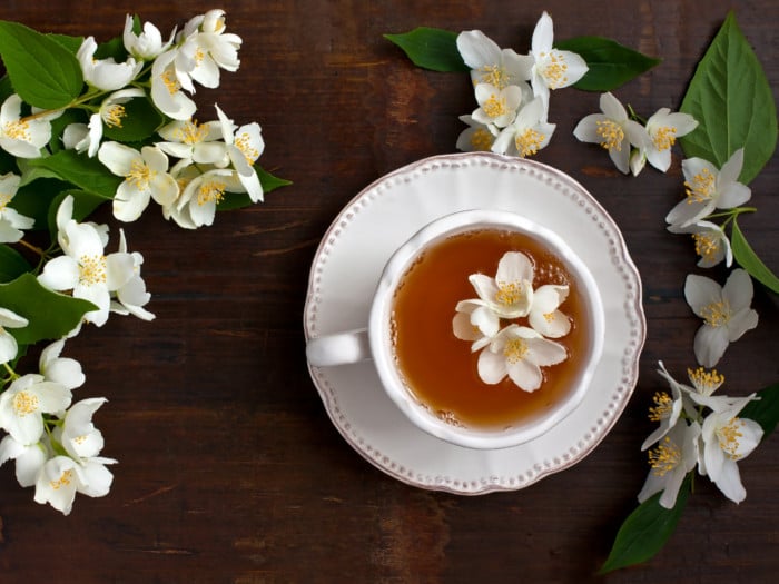 A cup with jasmine tea on a saucer, with fresh jasmine flowers next to it