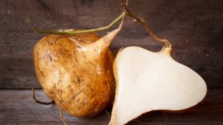 A close-up view of a whole and cut jicama on a wooden table