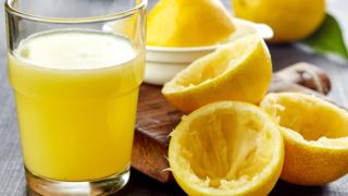 A glass of citrus juice next to squeezed citrus fruits and a juice squeezer at the back