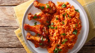Jollof rice with fried chicken wings close-up on a plate on a yellow napkin