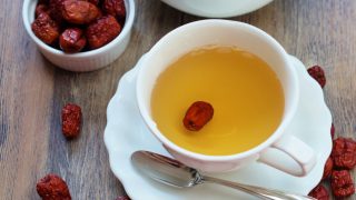 Jujube tea in a white cup placed on a wooden table, next to a small bowl filled with jujubes