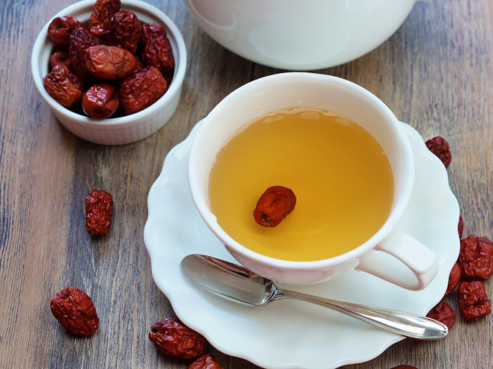 Jujube tea in a white cup placed on a wooden table, next to a small bowl filled with jujubes